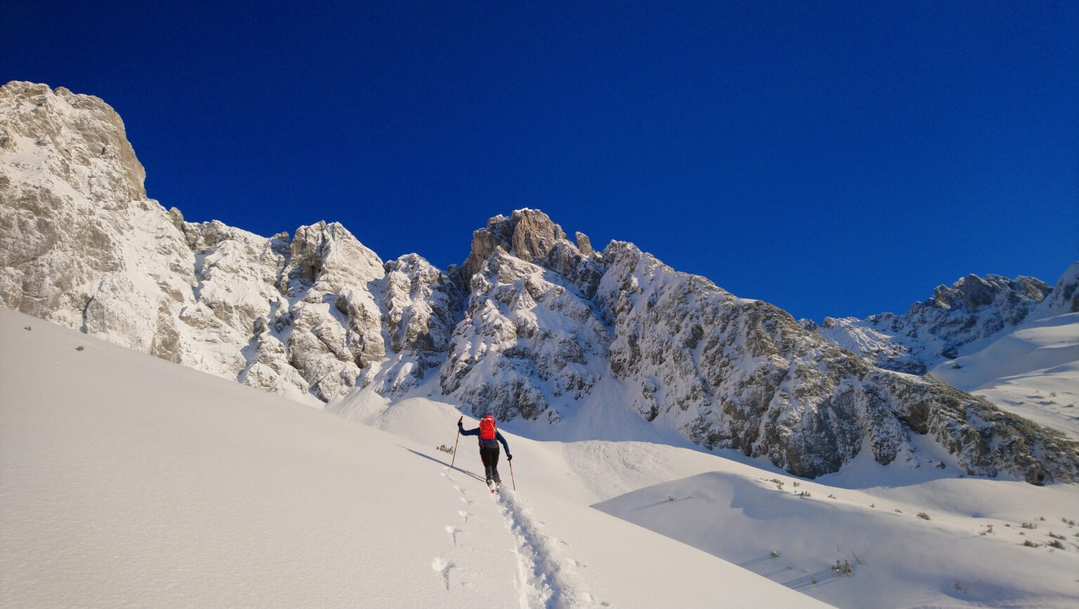 Skitourengeherin im Aufstieg unter den verschneiten Felswänden des Wilden Kaisers