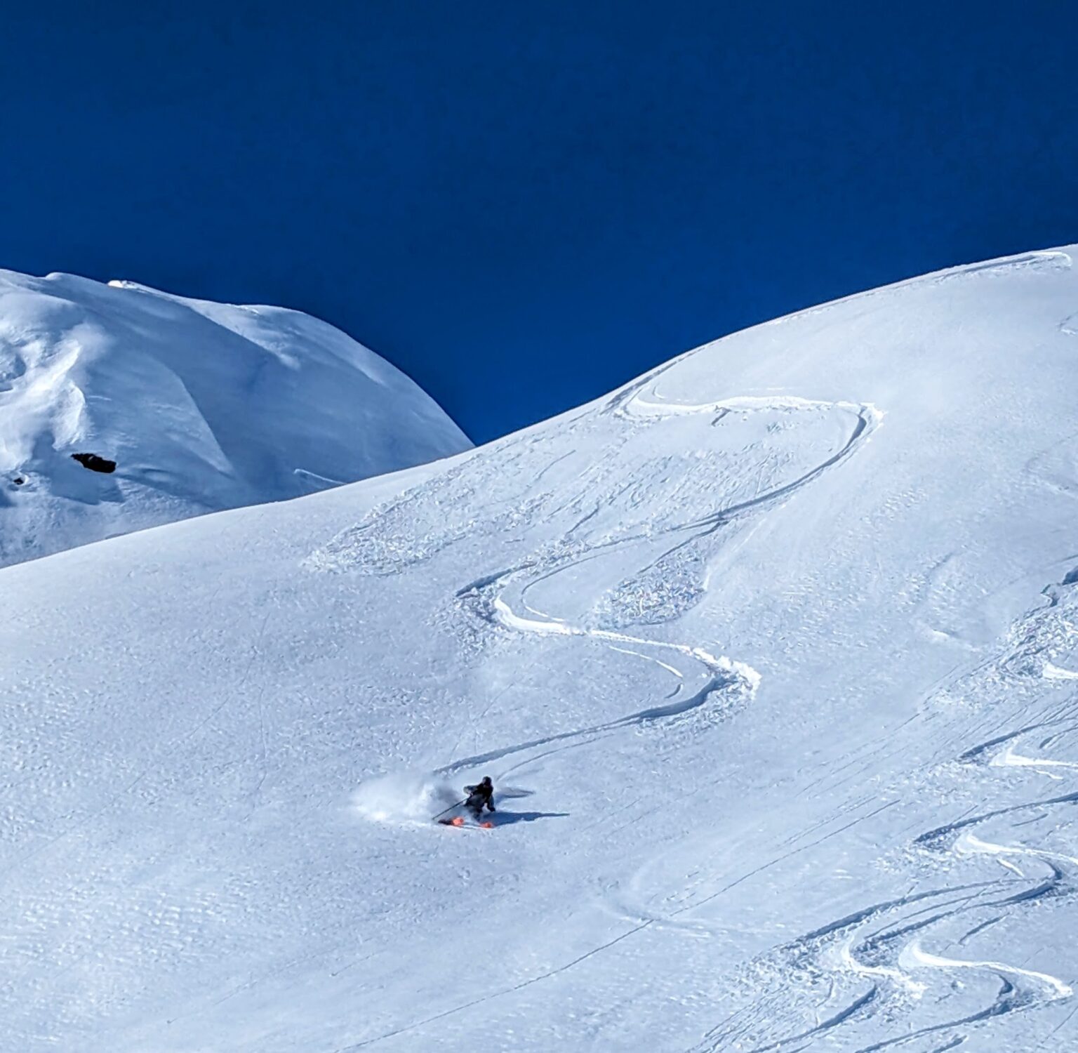 Skifahrer bei der Tiefschneeabfahrt mit Spuren im Pulverschnee